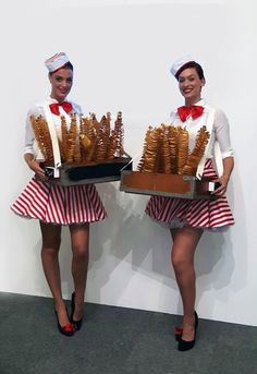 two women dressed in red and white holding trays of fried chicken nuggies