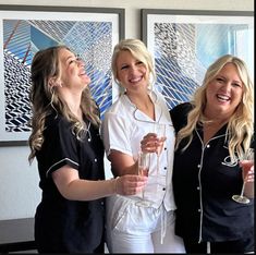 three beautiful women standing next to each other holding wine glasses