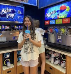 two girls are standing in front of some soda machines and one girl is holding a cup