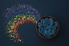 a wooden bowl filled with blue yarn next to a rainbow - colored object on a black surface