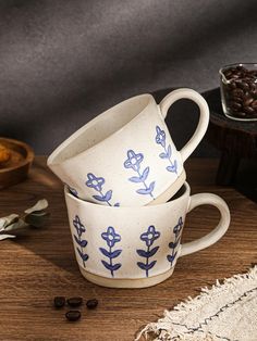 three coffee mugs sitting on top of a wooden table next to some dried beans