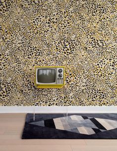 an old tv sitting on top of a rug in front of a leopard print wall