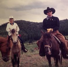 two men riding horses in the mountains on a cloudy day