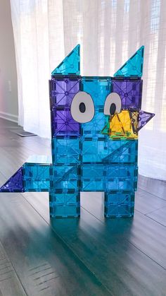 an origami cat made out of blue and purple blocks on a wooden floor