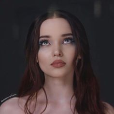 a woman with long brown hair and blue eyes is posing for a photo in front of a dark background