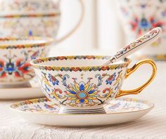 an ornately decorated tea cup and saucer set on a white tablecloth with gold trimmings