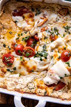 a casserole dish with tomatoes, cheese and herbs in it on a wooden table