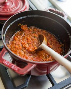 a pot filled with food sitting on top of a stove next to a wooden spoon