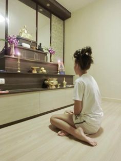 a woman sitting on the floor in front of a shelf with candles and other items