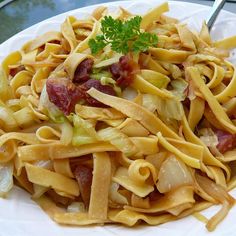 a white plate topped with pasta covered in sauce and bacon next to parsley on top of it