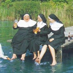 three women in black dresses are sitting on a dock and one is holding a beer