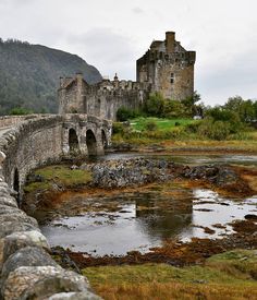 an old castle sits on top of a hill next to a small body of water