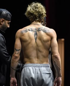 a man with a tattoo on his back standing next to another man in a suit