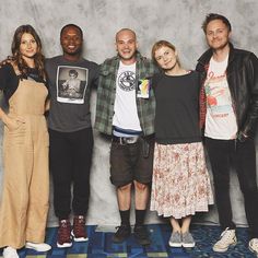 a group of people standing next to each other in front of a gray wall and blue carpet