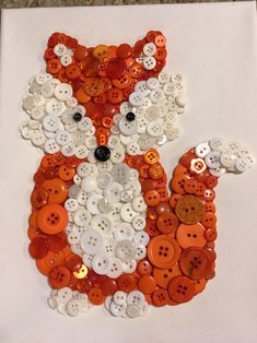 an animal made out of buttons sitting on top of a white piece of paper with the shape of a fox