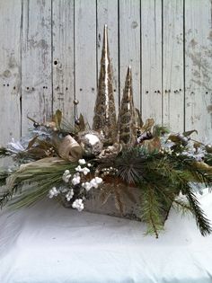 a white vase filled with flowers and greenery on top of a wooden table next to a fence