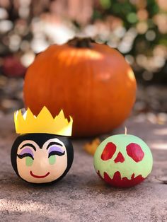 two pumpkins with faces painted on them sitting next to each other in front of a pumpkin