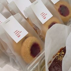 several pastries are in plastic containers with paper tags on the top one is filled with jelly and chocolate