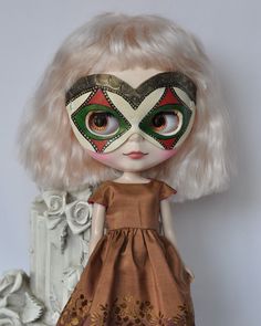 a doll with blonde hair wearing a masquerade and eye make up on her face