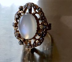 this ring is just incredible!! please see photos! crafted in solid heavy 14k yellow gold and very ornate plus dark enamel and real pearl seeds around!! the rest of enamel is present around the pearls and on the prongs! the pearls are all different in shape and size - because they are natural. all pearl seeds are present, no visible wear to the moonstone! the moonstone is clean and very chatoyant! )with strong chatoyancy effect! - which moves from one side to another as you move your hand!) ! the Antique Oval Moonstone Ring Collectible, Collectible Oval Cabochon Moonstone Ring, Antique Oval Moonstone Ring, Gold Cabochon Moonstone Ring Collectible, Heirloom Gold Moonstone Oval Cabochon Ring, Victorian Oval Cabochon Pearl Ring, Antique White Oval Moonstone Ring, Victorian Oval Cabochon Moonstone Ring, Heirloom Gold Moonstone Ring Oval Cabochon