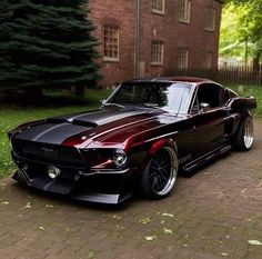 a black and red mustang parked in front of a brick building with trees around it