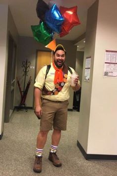 a man is standing in an office hallway wearing a hat and suspenders with balloons attached to his head