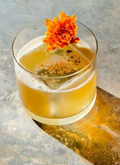 an orange flower sitting on top of a drink in a glass filled with ice and liquid