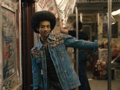 a man with an afro standing on a subway train next to other people and looking at the camera