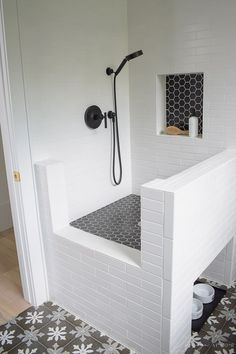 a white tiled bathroom with black and white floor tiles on the walls, shower head, and hand held faucet