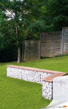 a stone bench sitting in the middle of a lush green field next to a wooden fence