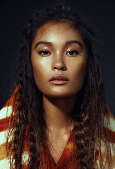 a woman with long hair wearing a sweater and looking at the camera while standing in front of a black background