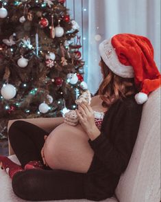 a pregnant woman sitting on a couch in front of a christmas tree