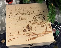 a wooden box with a snowman on it and christmas tree in the background that says george's christmas eve box