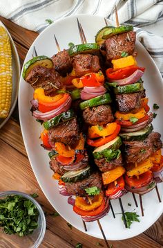 a white plate topped with meat and veggies next to corn on the cob