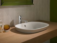 a white sink sitting on top of a wooden counter next to a green mirror above it