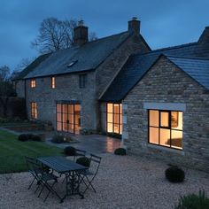 a house that is lit up at night with lights on the windows and tables outside