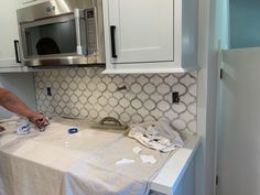 a woman is painting the backs of cabinets in a kitchen with white walls and countertops