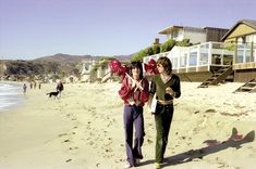 two women walking on the beach with houses in the background