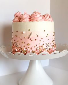 a pink and white cake with gold sprinkles on it sitting on a plate