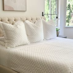 a bed with white quilts and pillows in a bedroom next to a large window