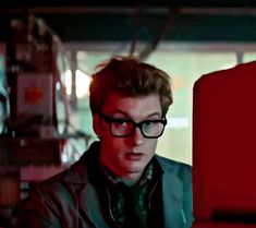 a young man wearing glasses looking at a computer screen in a room with red walls