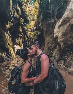 a man and woman kissing while standing in the water near a cliff face each other