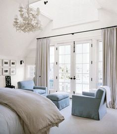 a bedroom with white walls and blue chairs in front of the bed, chandelier