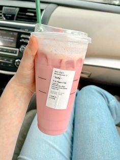 a person holding up a pink drink with a green straw in their hand while sitting in a car