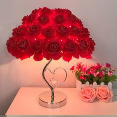 a heart shaped lamp sitting on top of a table next to pink flowers and a vase