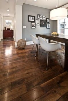 a dining room table with white chairs and pictures on the wall behind it in an open floor plan