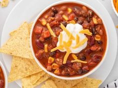 a bowl of chili with sour cream and tortilla chips next to it on a plate