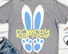 a gray shirt with blue and green bunny ears on it, next to some shoes