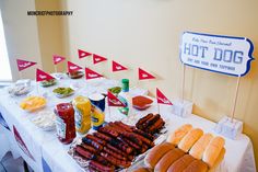 hot dogs and buns are on the table at a party with flags in the background