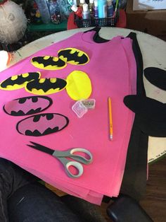 a pink shirt with batman cutouts on it and scissors next to the t - shirt